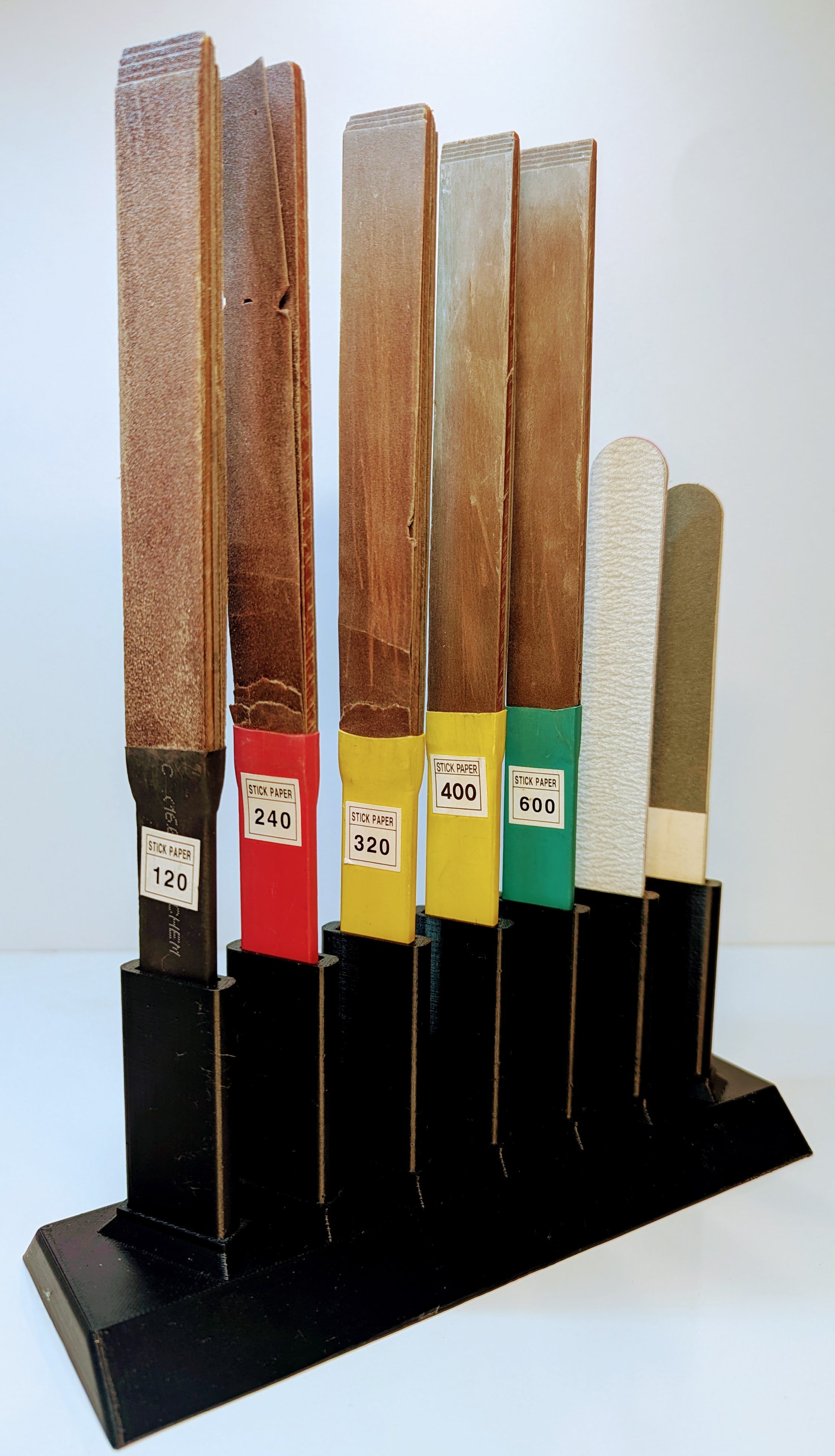Set of sanding sticks with different grits on a black stand against a white background