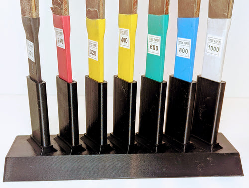 Set of sandpaper sticks in various grits in a black holder on a white background